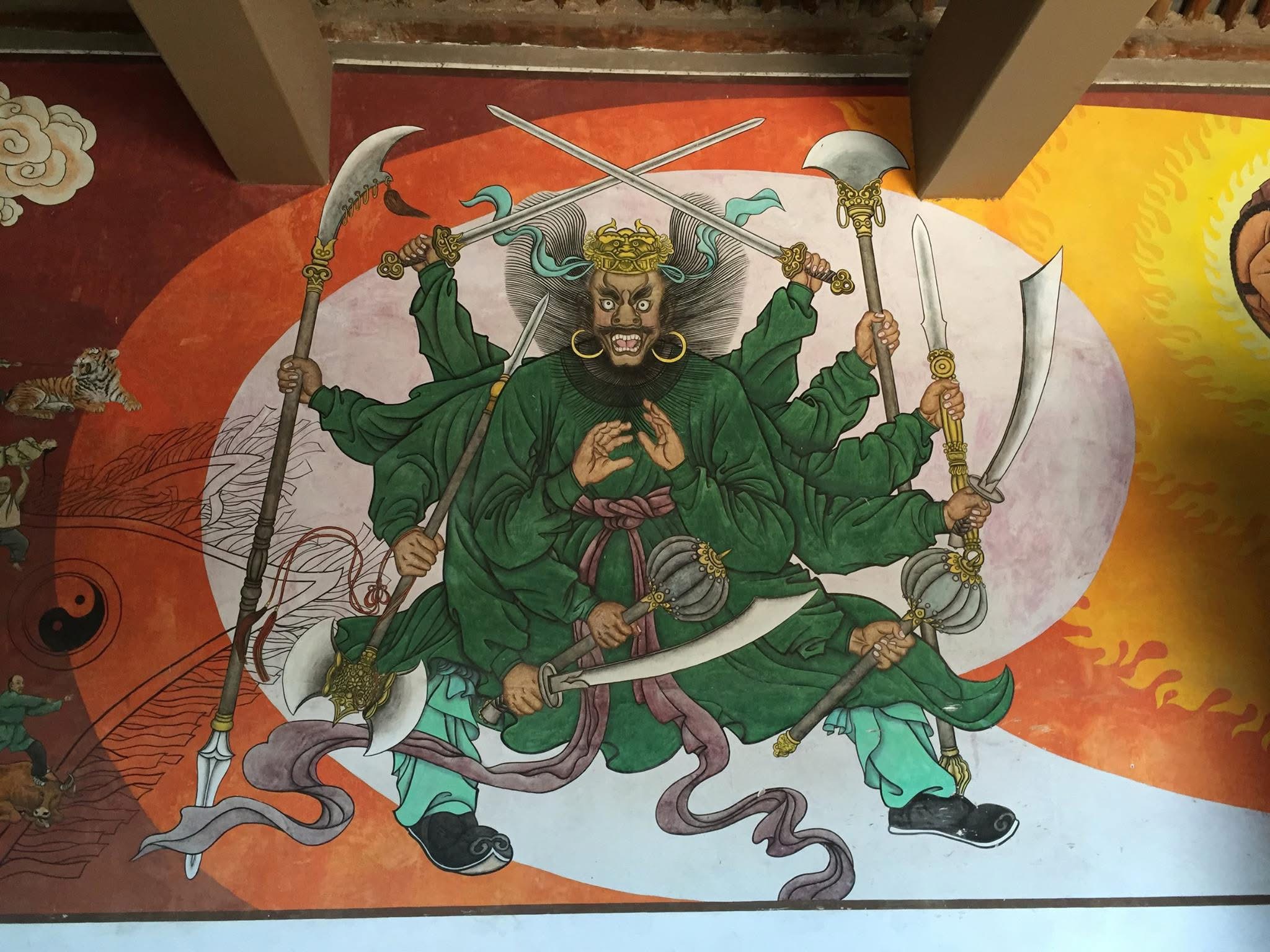 Temple mural of a multi-armed martial guardian holding traditional Chinese weapons